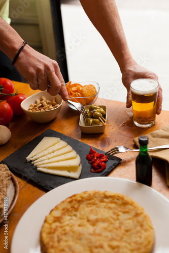Vertical Spanish tapas bar table with various typical dishes and beer with hands acting.  