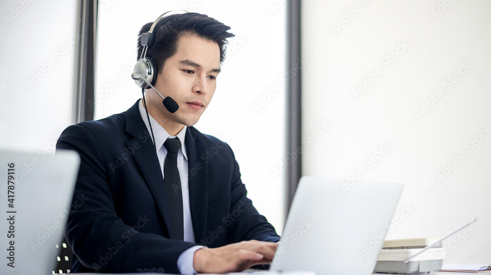Asian man wearing headphones working as a call center in an office. Asian man wearing headphones working as a call center in an office.