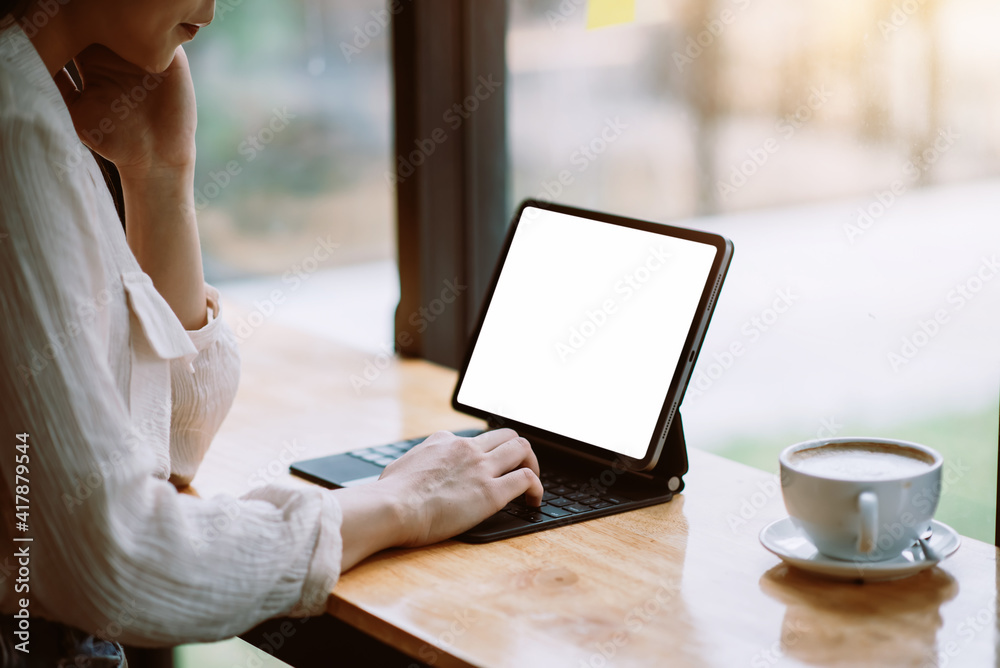 Mock up. Woman hand printing on the tablet blank screen. Coffee mug placed at the office table. Mock up. Woman hand printing on the tablet blank screen. Coffee mug placed at the office table.