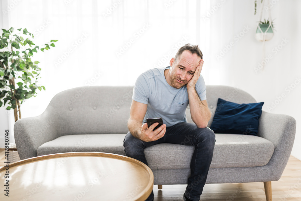 Fototapeta premium A sad man using smartphone at home