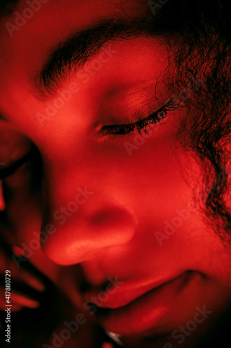 Close up face. Beautiful african-american woman's portrait isolated on red studio background in neon, monochrome. Concept of human emotions, facial expression, sales, ad, fashion and beauty.