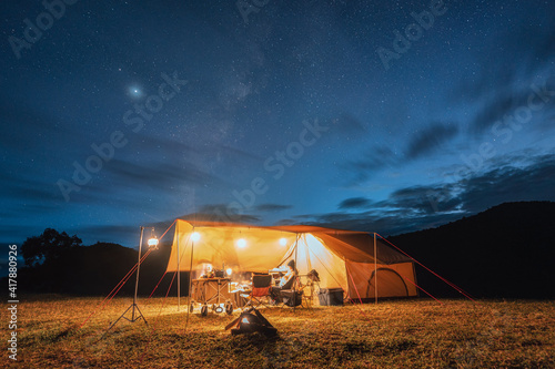 Tourists in yellow tent camping on hill with milky way in the night sky