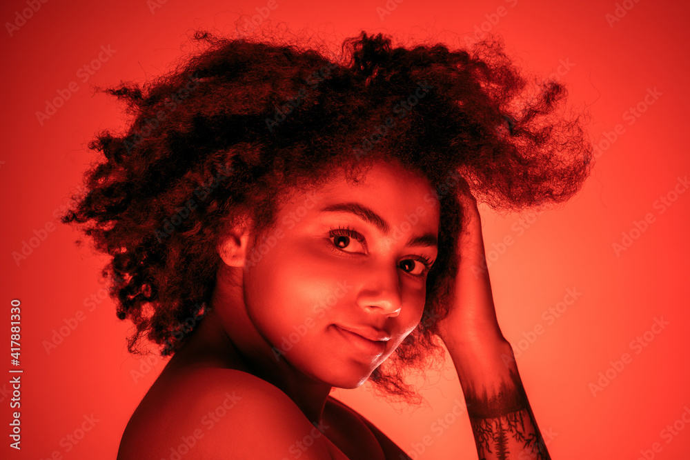 Dancing. Beautiful african-american woman's portrait isolated on red studio background in neon, monochrome. Concept of human emotions, facial expression, sales, ad, fashion and beauty. Dancing. Beautiful african-american woman's portrait isolated on red studio background in neon, monochrome. Concept of human emotions, facial expression, sales, ad, fashion and beauty.
