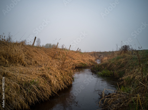 Close up of Small River Early Morning in Heavy Fog Next to a Green Field