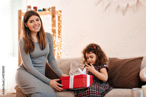 Smiling woman in dress giving gift to child. Little birthday girl posing with mother.