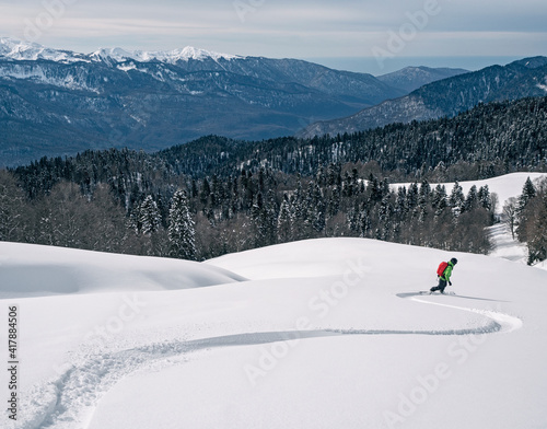 Active man riding snowboard on powder snow at mountains and wood background in Krasnaya Polyana resort in Russia