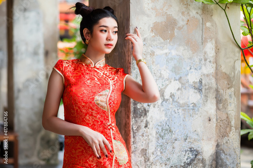 A beautiful Thai woman wearing a Chinese red cheongsam is standing in a corridor inside an old cement building. photo