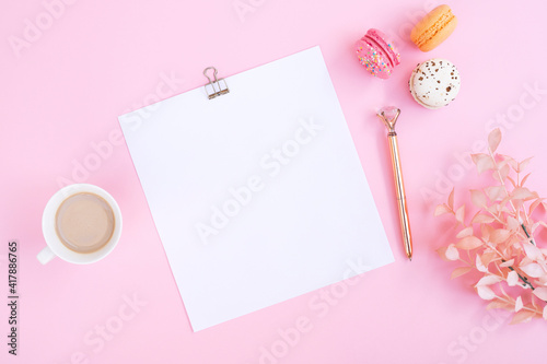 Notebook, cup of coffee and colorful macaron on pastel pink desk top view. Cozy morning breakfast. Fashion flat lay. Sweet macaroons. © Hazal
