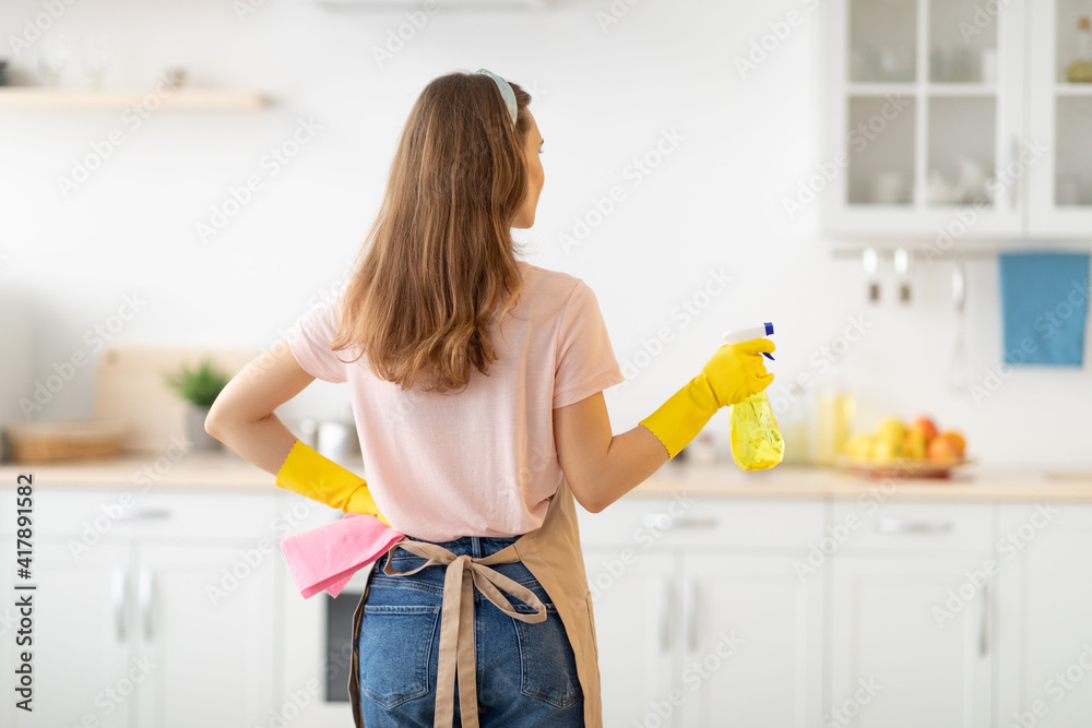 Back view of young lady with cleaning spray ready to tidy her apartment, blank space Back view of young lady with cleaning spray ready to tidy her apartment, blank space