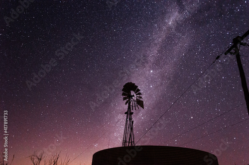 Molino de viento en campo con cielo estrellado y vía láctea