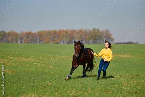 Young woman running with horse on green field on sunny summer day, copy space. Girl training bay stallion outdoors © mirage_studio