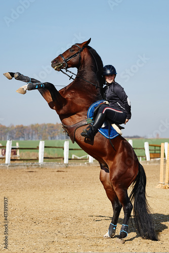 Young woman and beautiful sorrel stallion rearing up in paddok outdoors, copy space. Equestrian sport.