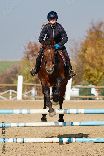 Young horsewoman on brown horse overcomes an obstacle outdoors, copy space. Equestrian sport, jumping. © mirage_studio