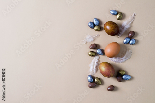Festive Easter minimalist background. Natural brown eggs lie on a beige background, candy jelly, almonds in chocolate of different colors lie nearby. Copying space, flat layout