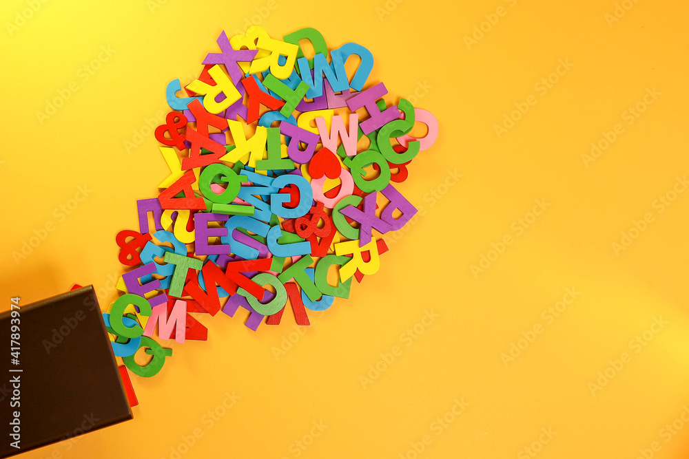 Fototapeta premium Colorful block letters flowing out from the wooden box on the yellow background 