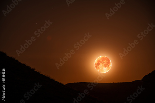 Amazing full red moon in the night sky illuminates hills silhouette. Night photography