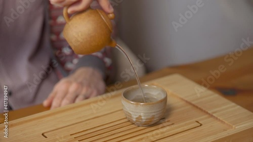 Close-up of man pouring Chinese tea. Art. Traditional Chinese tea with small teapot on wooden tray. Tea ceremony for one person photo