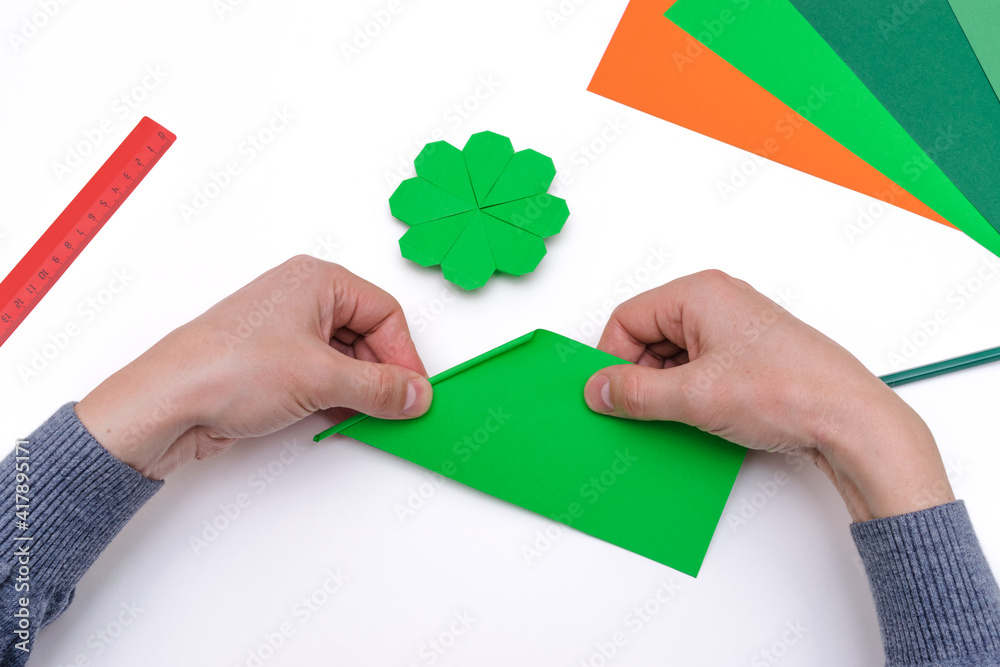 Men's hands fold a clover leaf from green paper in the origami technique on a white background.Process of making,step-by-step instructions, step 23. Concept of the St.Patrick's Day. Men's hands fold a clover leaf from green paper in the origami technique on a white background.Process of making,step-by-step instructions, step 23. Concept of the St.Patrick's Day.