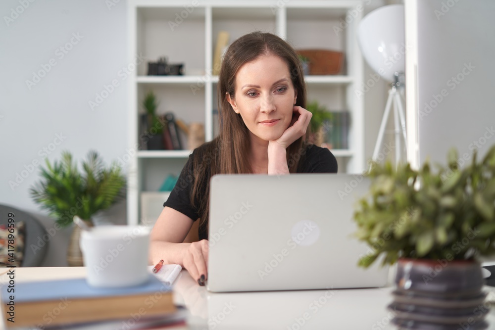 Image of young happy white business woman sitting at office desk, working from home, using laptop computer, having video chat. Image of young happy white business woman sitting at office desk, working from home, using laptop computer, having video chat.