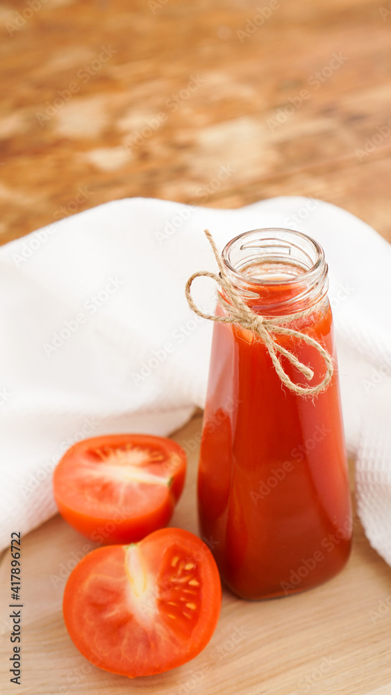 Tomato juice in glass bottle and fresh tomatoes on wooden cutting board and white towel Tomato juice in glass bottle and fresh tomatoes on wooden cutting board and white towel