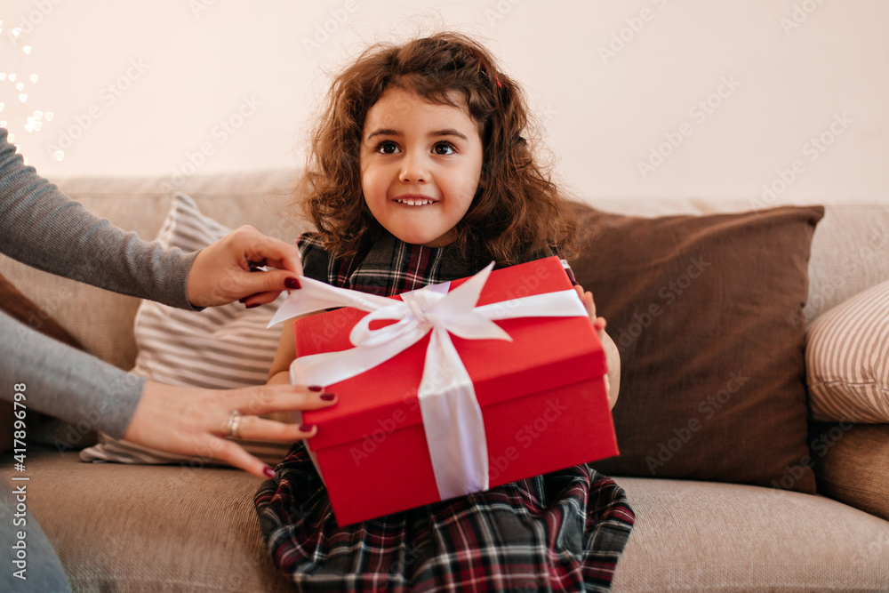 Funny little kid holding birthday present. Curly preteen girl with gift sitting on sofa. Funny little kid holding birthday present. Curly preteen girl with gift sitting on sofa.