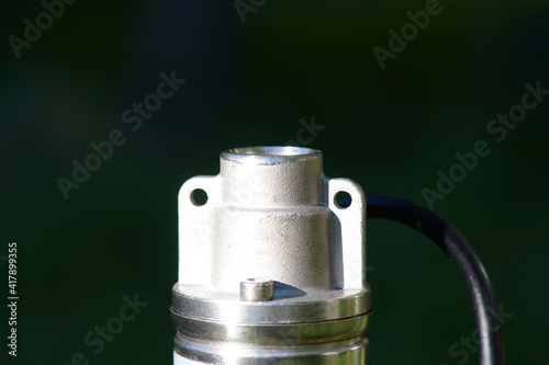 Top of the pump with black cable on a dark green background. Borehole pump outlet thread. The top of the well pump with lugs for fastening with a cable. The pump is in bright sunlight.