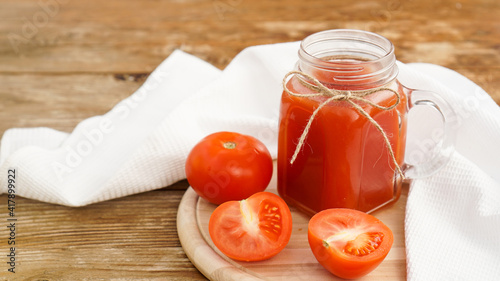 Tomato juice in glass jar and fresh tomatoes on wooden cutting board and white towel