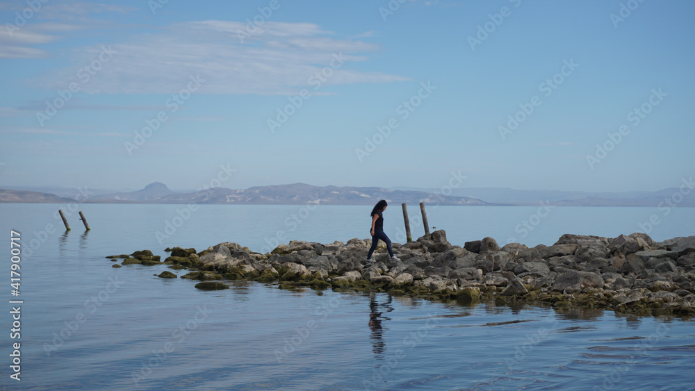 Mujer caminando sobre rocas a la orilla de un lago