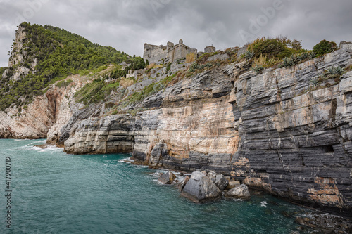 Beautiful seascape. Stormy sea on a windy day: blue waves breaks on the stone shore of Porto Venere with Doria Castle (12th century) on the top of mountain