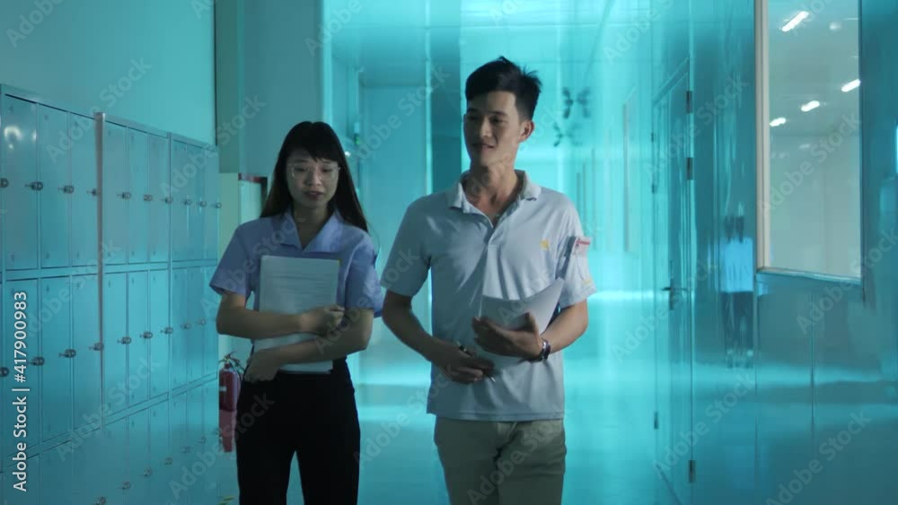 Man and woman walking down blue-lit hallway. Camera tracks right