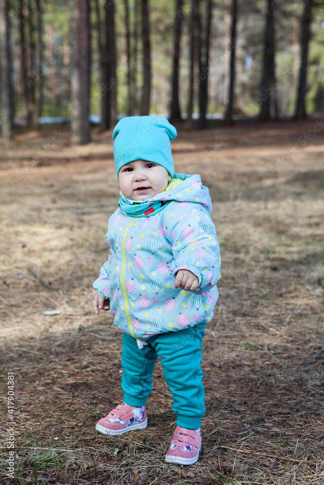 Toddler child standing alone in spring forests, wearing blue hat, jacket and trousers Toddler child standing alone in spring forests, wearing blue hat, jacket and trousers