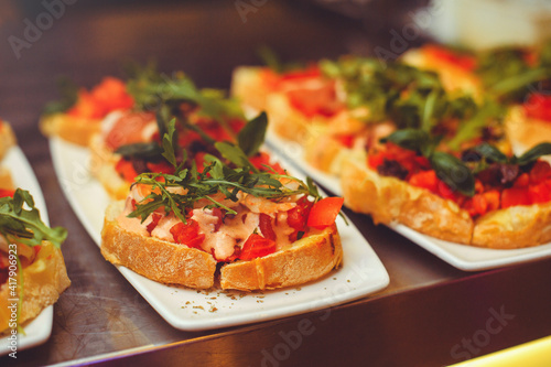 bruschetta with shrimps, basil, pesto and mozzarella sauce and tomato on a white plate on a wooden background. Italian restaurant. close-up of food