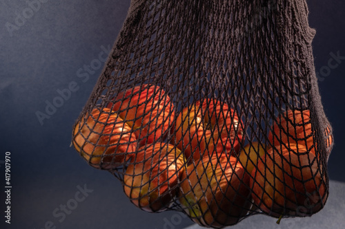 Juicy red apples in a dark blue string bag on a gray blue background in the sunlight. Healthy lifestyle. Eco-friendly package. photo