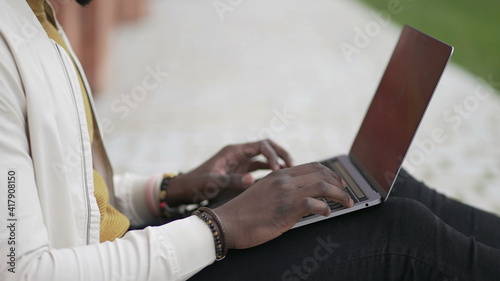 African man in front of laptop computer working remotely outside.