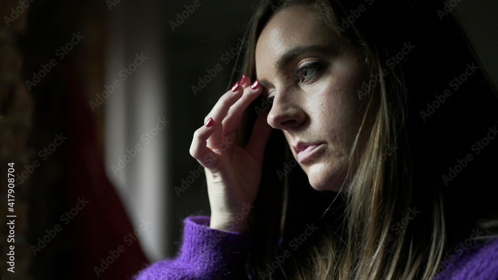 Anxious young woman standing by window concerned with life problems Anxious young woman standing by window concerned with life problems