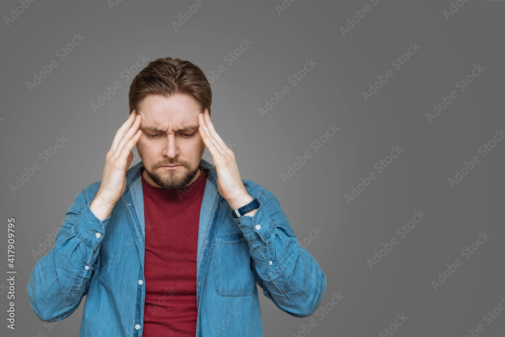 A young European bearded young man keeps his head in tension, stress, on a gray background to copy the space. Negative human emotions and feelings A young European bearded young man keeps his head in tension, stress, on a gray background to copy the space. Negative human emotions and feelings