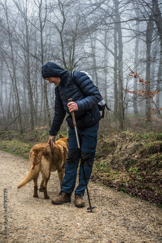 A man hiker petting his pet on a walk in nature. Rainy day on winter or fall. Forest with trees on the background. 