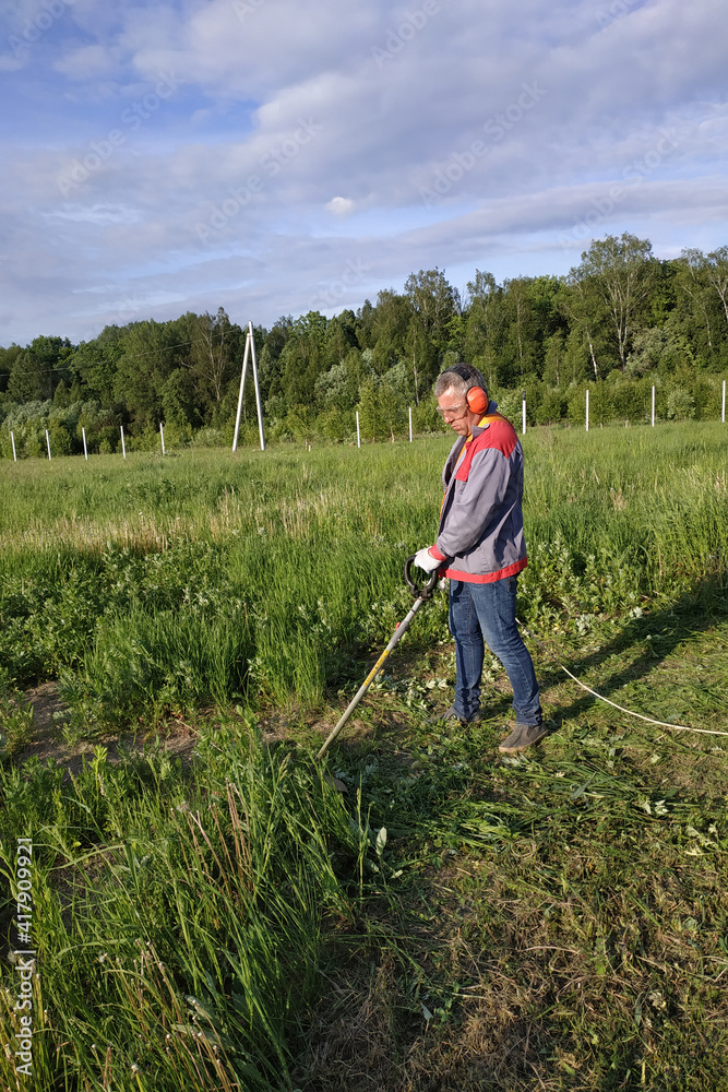 Man mows the grass with a trimmer, tall grass in a meadow, handmade in the garden. Man mows the grass with a trimmer, tall grass in a meadow, handmade in the garden.
