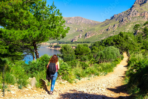 A young girl walking hiking on a path on a beautiful mediterranean forest along the coast of balearic island of Mallorca with the mountains at the background