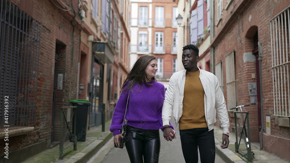Diversity concept. Interracial couple holding hands walking outside in european street