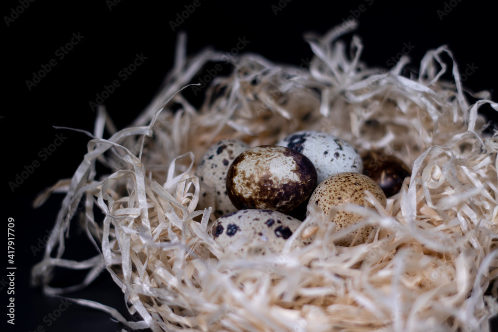 Obraz premium Heap of Quail eggs in nest from dry grass or hay isolated on dark background. copy space for advertising of food or restaurant menu design. easter eggs