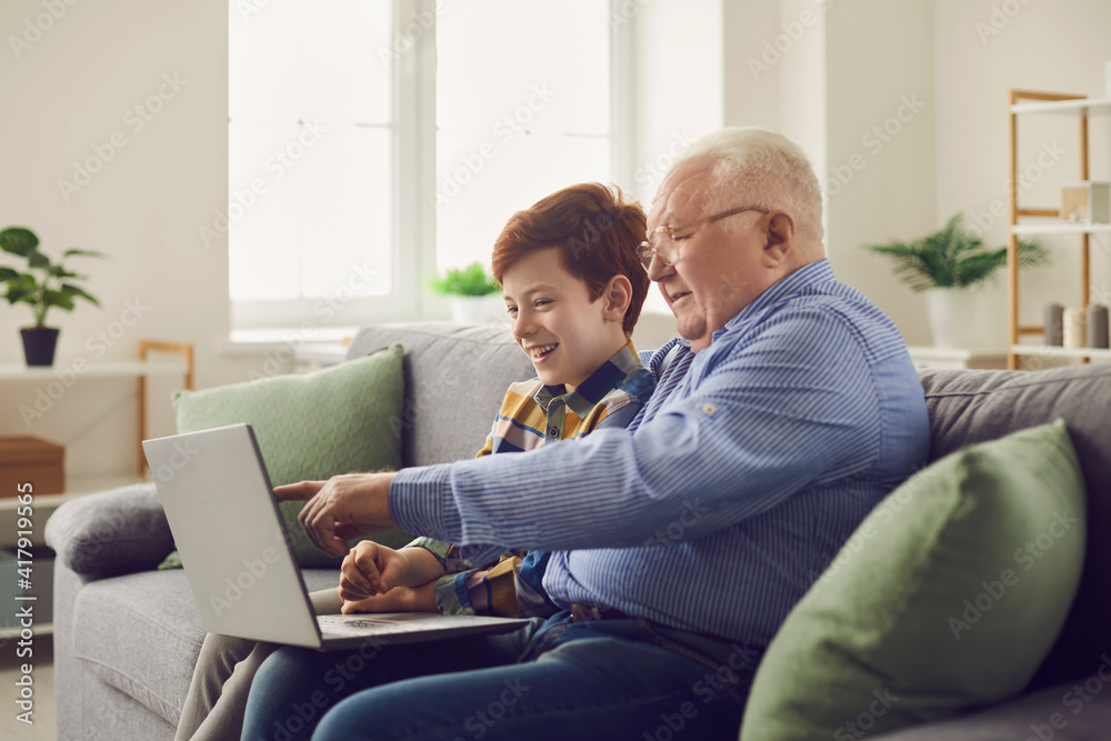 Happy family using modern technology. Smiling grandfather and grandson sitting with laptop computer on cozy sofa at home, enjoying good wifi connection, browsing Internet and watching movies together Happy family using modern technology. Smiling grandfather and grandson sitting with laptop computer on cozy sofa at home, enjoying good wifi connection, browsing Internet and watching movies together