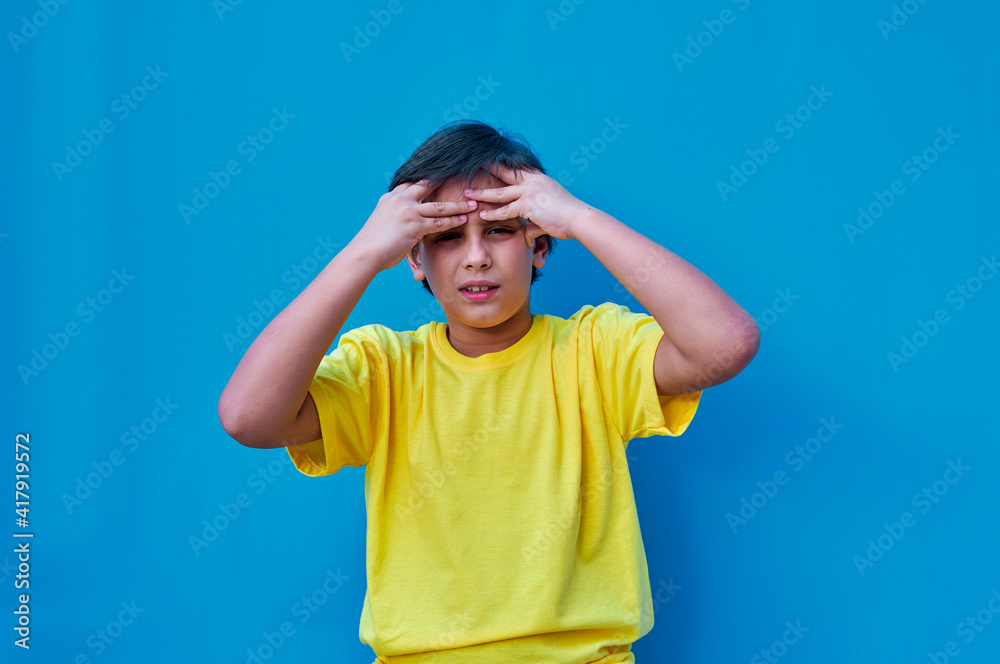 Portrait of boy with worried face in yellow t-shirt, on blue background. Copy space Portrait of boy with worried face in yellow t-shirt, on blue background. Copy space