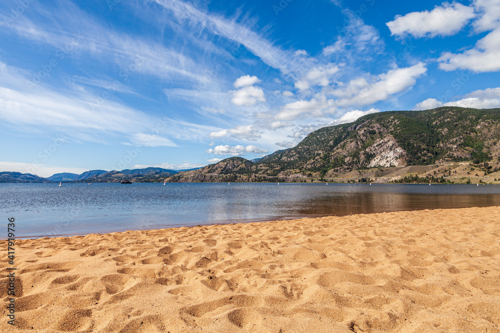 view o from the yellow sand beach to calm lake with mountains and cloudy sky