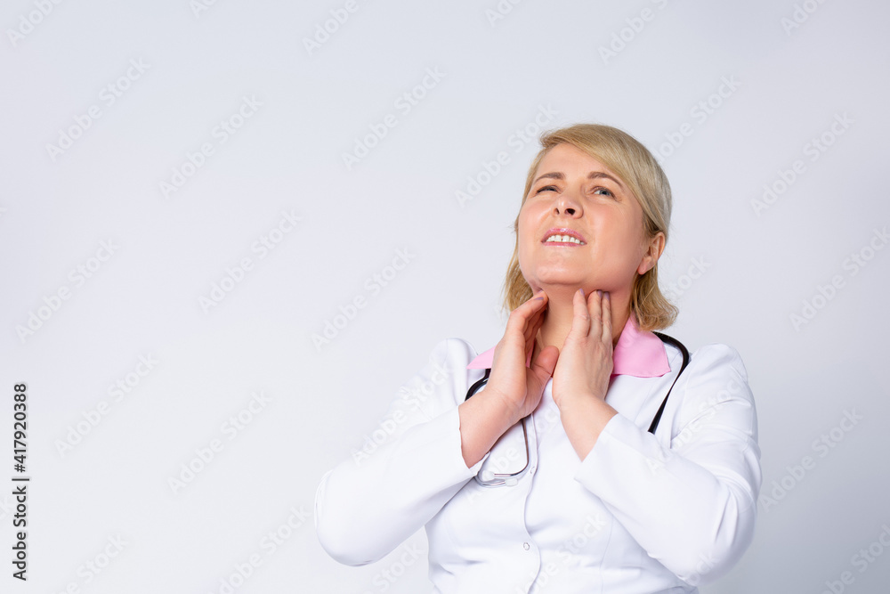Sick mid-aged female doctor complaining about sore throat on white background with plenty side for medicine advertisement and publicity Sick mid-aged female doctor complaining about sore throat on white background with plenty side for medicine advertisement and publicity