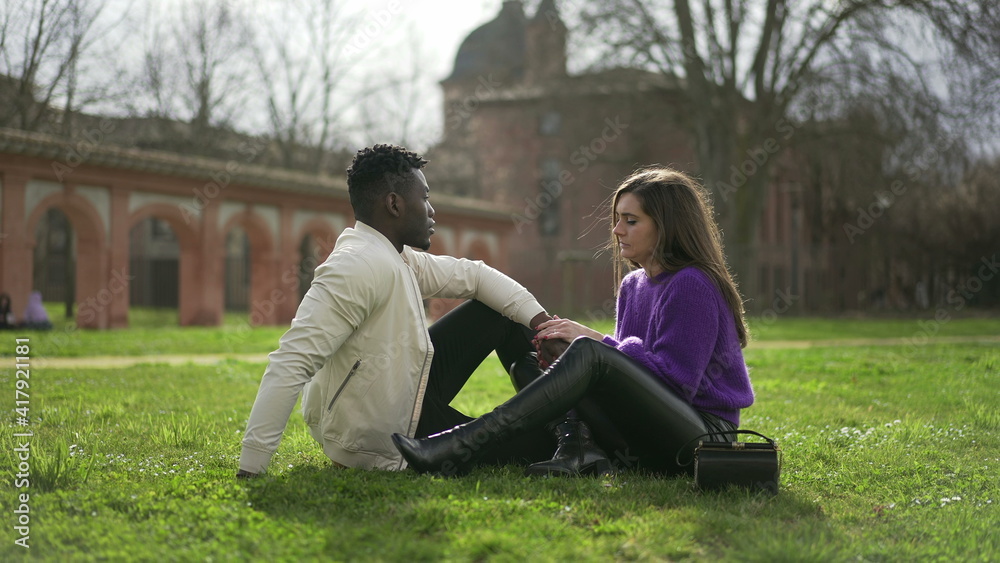 Interracial couple hanging together outside sitting on grass at park Interracial couple hanging together outside sitting on grass at park
