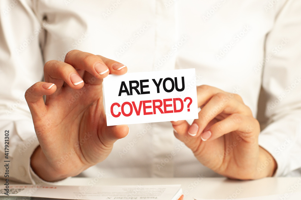 A woman in a white shirt holds a piece of paper with the text: ARE YOU COVERED. Business concept. A woman in a white shirt holds a piece of paper with the text: ARE YOU COVERED. Business concept.
