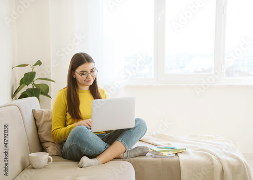Young attractive woman student study online with laptop, sitting on sofa at home. Distance learning and remote teaching concept with text place.