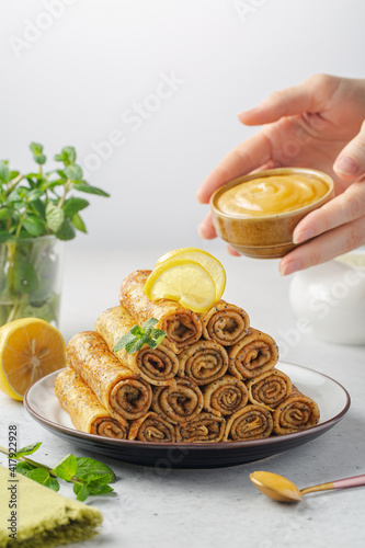 Sweet crepe roll-ups with poppy seeds and woman hands holding a lemon curd. Light background. photo