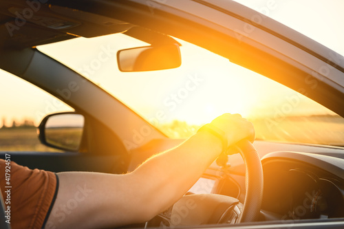 Caucasian Man in automobile in the countryside and sun rays. Male driver driving a car at sunset background. Summer travel, road trip and vacations concept